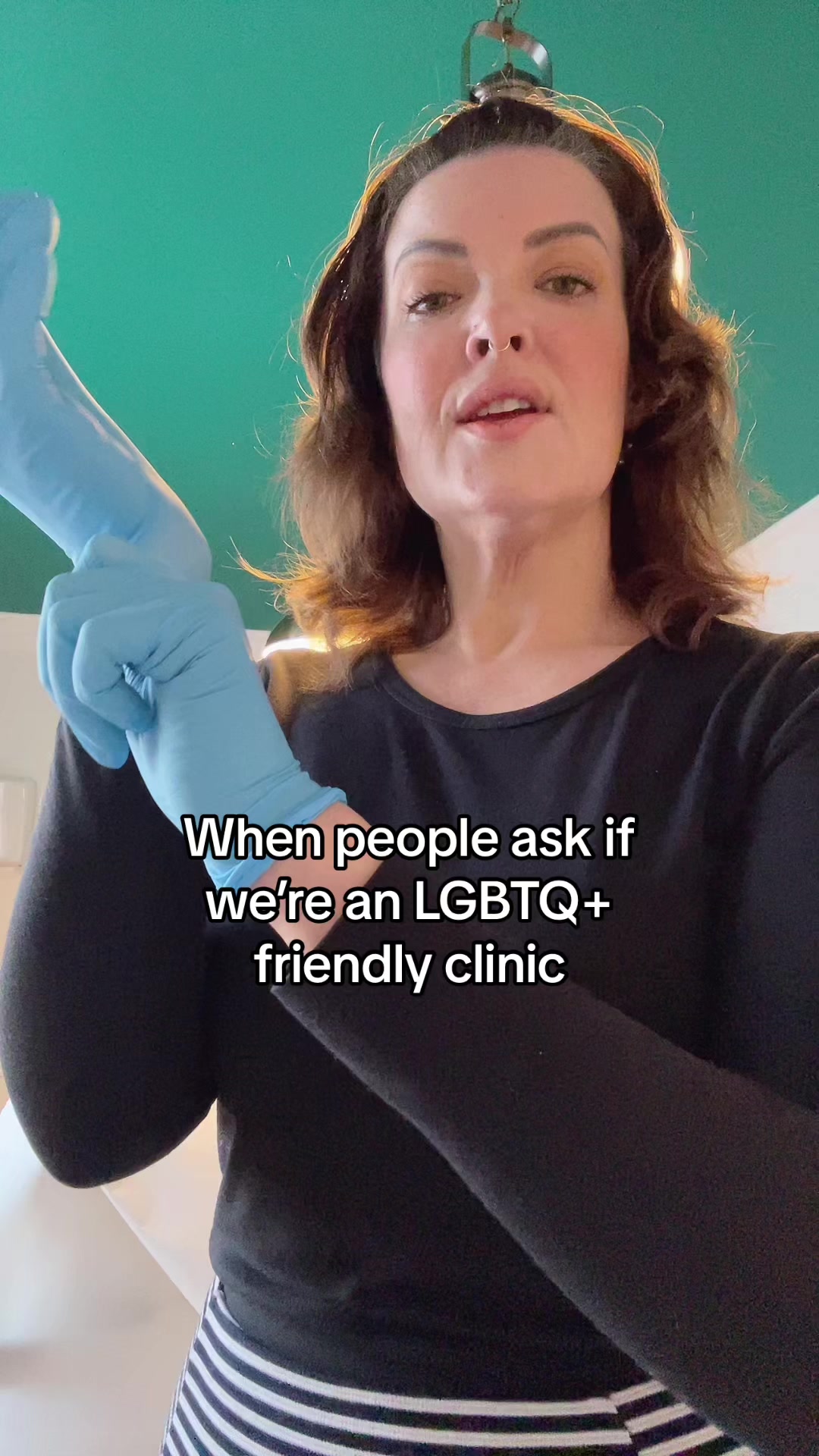 Helen in the clinic pulling on blue examination gloves under the teal ceiling